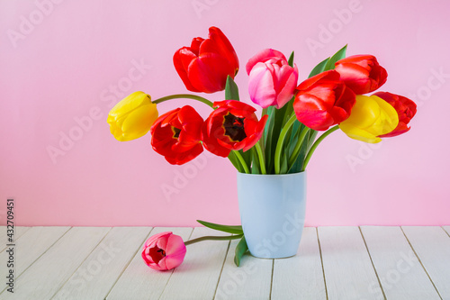 Beautiful bouquet of tulips in a vase on a white wooden table on a pink background