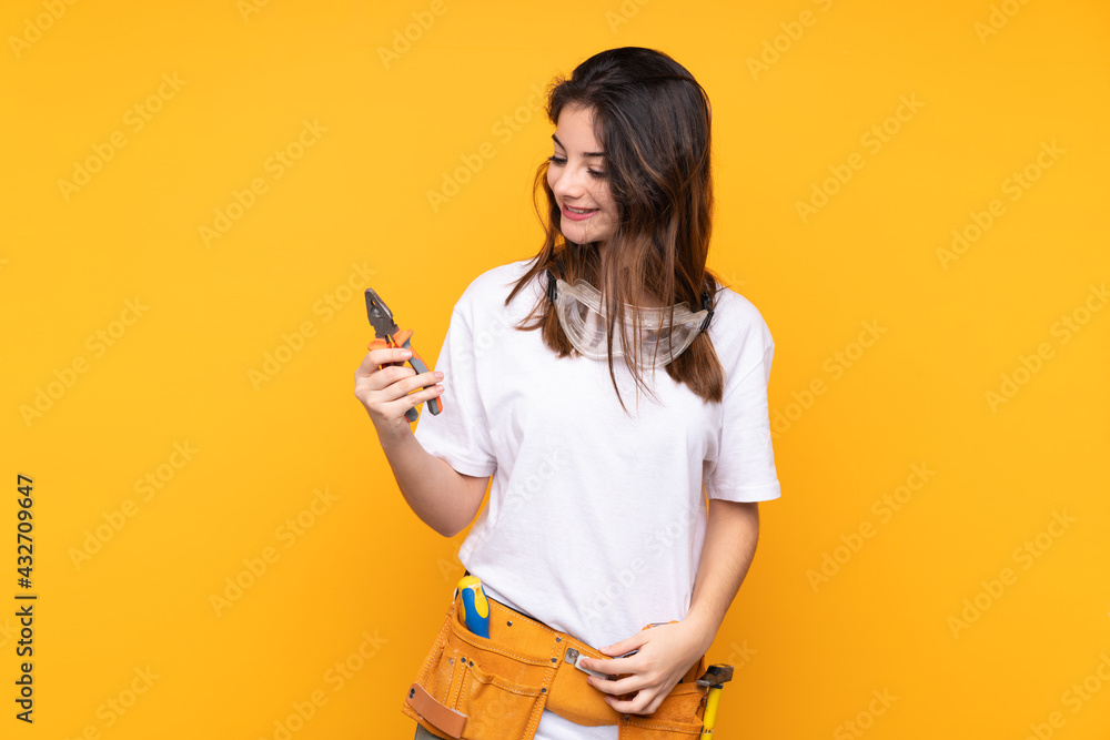 Young electrician woman over isolated on yellow background Young electrician woman over isolated on yellow background
