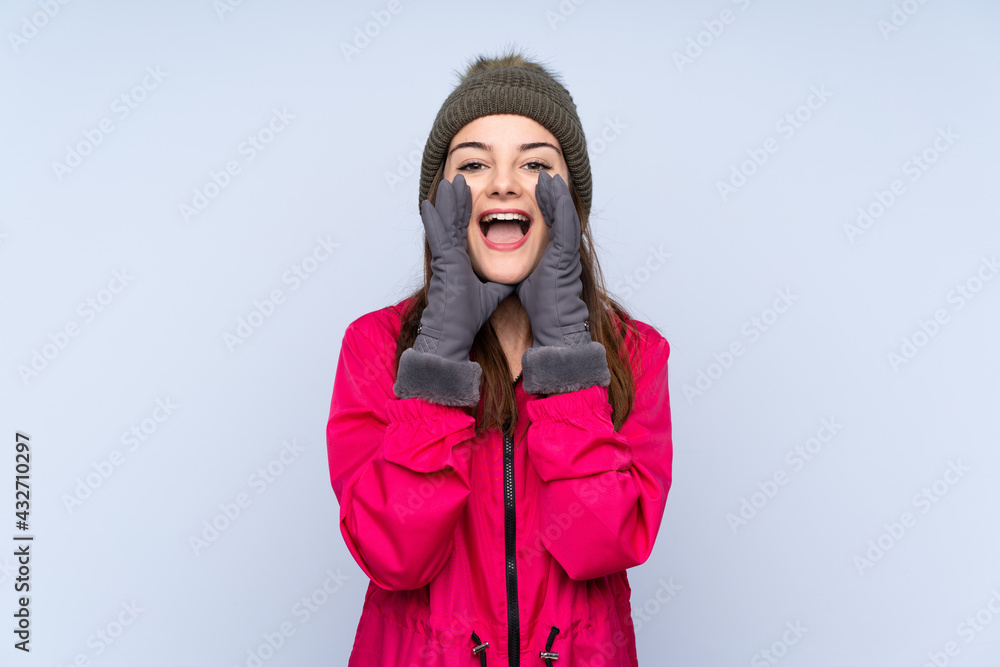 Young girl with winter hat isolated on blue background shouting and announcing something Young girl with winter hat isolated on blue background shouting and announcing something