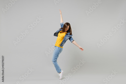 Full length side view young caucasian woman in casual denim jacket yellow t-shirt looking aside leaning back stand on toes dancing isolated on grey background studio portrait People lifestyle concept.