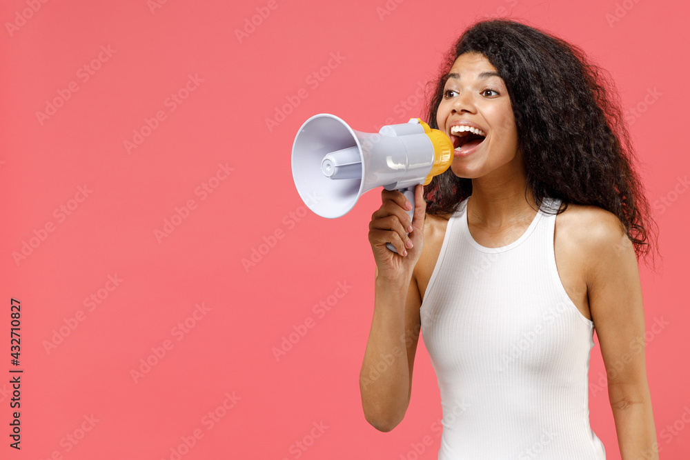 Young fun expressive excited happy curly african american woman 20s wearing casual white tank shirt screaming shouting loudly hot news in megaphone isolated on pink color background studio portrait. Young fun expressive excited happy curly african american woman 20s wearing casual white tank shirt screaming shouting loudly hot news in megaphone isolated on pink color background studio portrait.