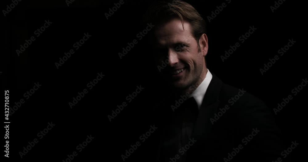 businessman wearing a cool tuxedo is smiling and looking around in a dark studio businessman wearing a cool tuxedo is smiling and looking around in a dark studio