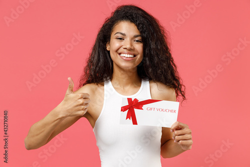 Young smiling excited happy satisfied african american woman 20s in casual white tank shirt hold in hand gift voucher flyer mock up dshow thumb up gesture isolated on pink background studio portrait.