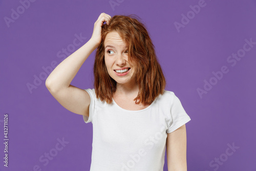 Young sad puzzled troubled pensive thoughtful confused caucasian woman 20s in white basic blank print design t-shirt look aside scratch hold head isolated on dark violet background studio portrait photo