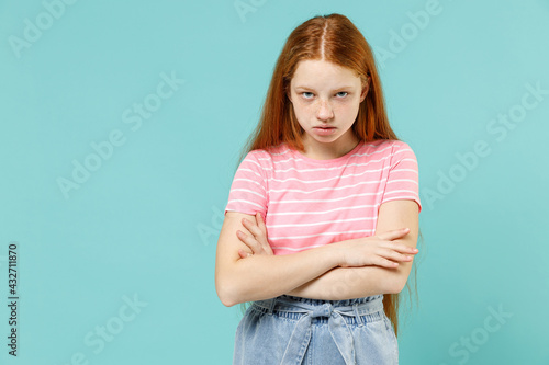 Obraz na plátně Little frowning angry redhead kid girl 12-13 year old wear pink striped t-shirt hold hands arms crossed folded isolated on pastel blue background studio portrait