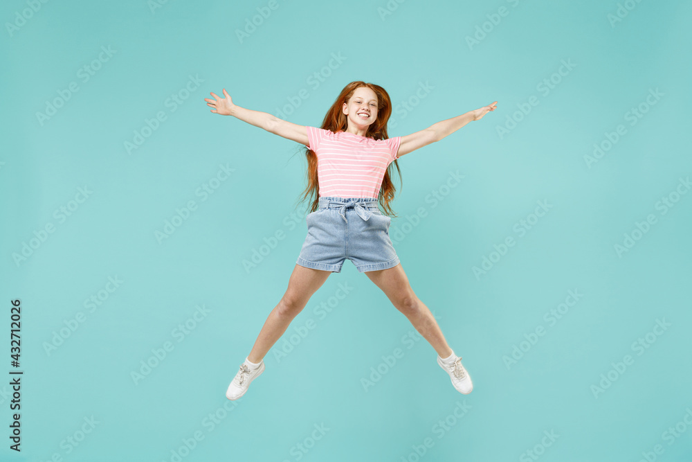 Full length little fun overjoyed happy redhead kid girl 12-13 year old in pink striped t-shirt with outstretched hands isolated on pastel blue background studio Children lifestyle childhood concept.