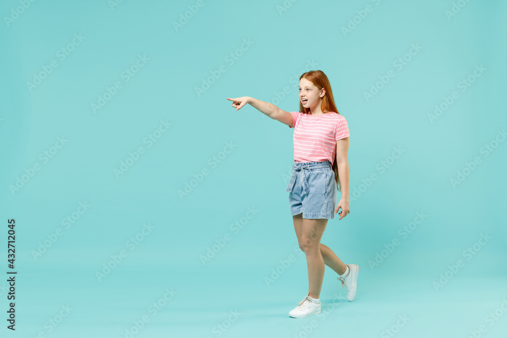 Full length little redhead kid girl 12-13 year old in pink striped tshirt point index finger aside on copy space mock up isolated on pastel blue background studio Children lifestyle childhood concept Full length little redhead kid girl 12-13 year old in pink striped tshirt point index finger aside on copy space mock up isolated on pastel blue background studio Children lifestyle childhood concept