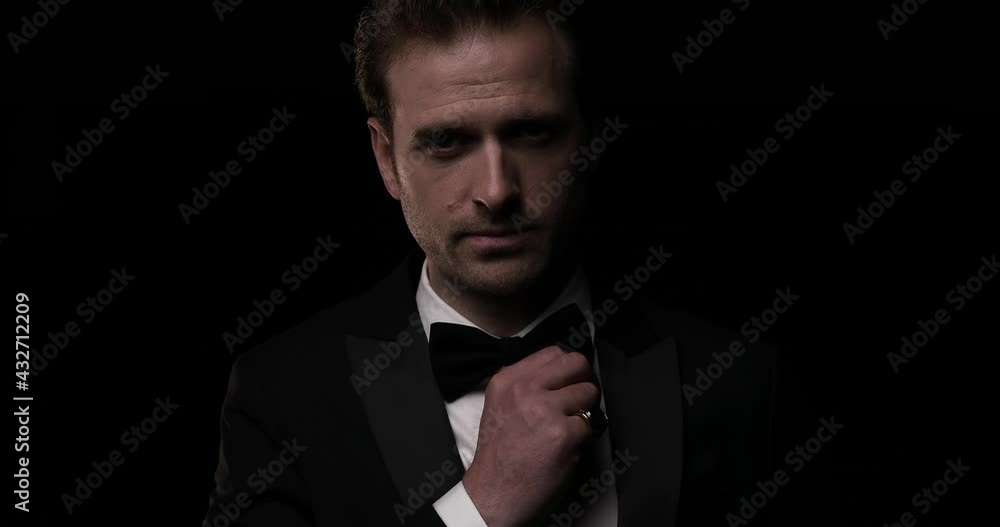 young elegant fashion model fixing his bowtie and smiling at the camera against black studio background young elegant fashion model fixing his bowtie and smiling at the camera against black studio background