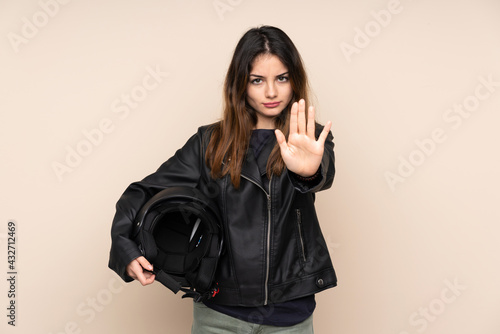 Woman with a motorcycle helmet isolated on beige background making stop gesture with her hand © luismolinero