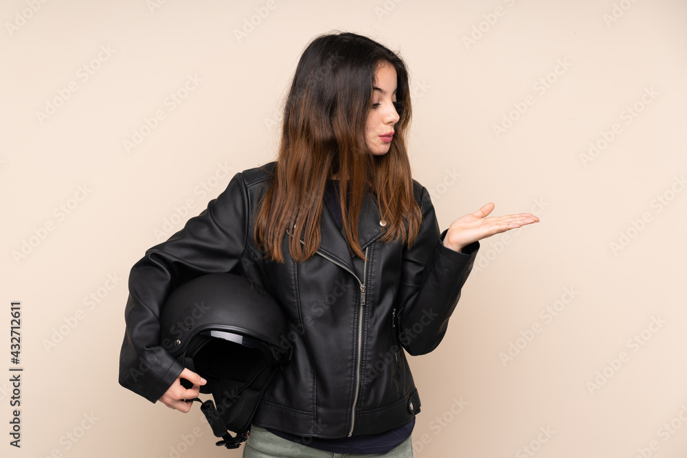 Woman with a motorcycle helmet isolated on beige background holding copyspace imaginary on the palm Woman with a motorcycle helmet isolated on beige background holding copyspace imaginary on the palm