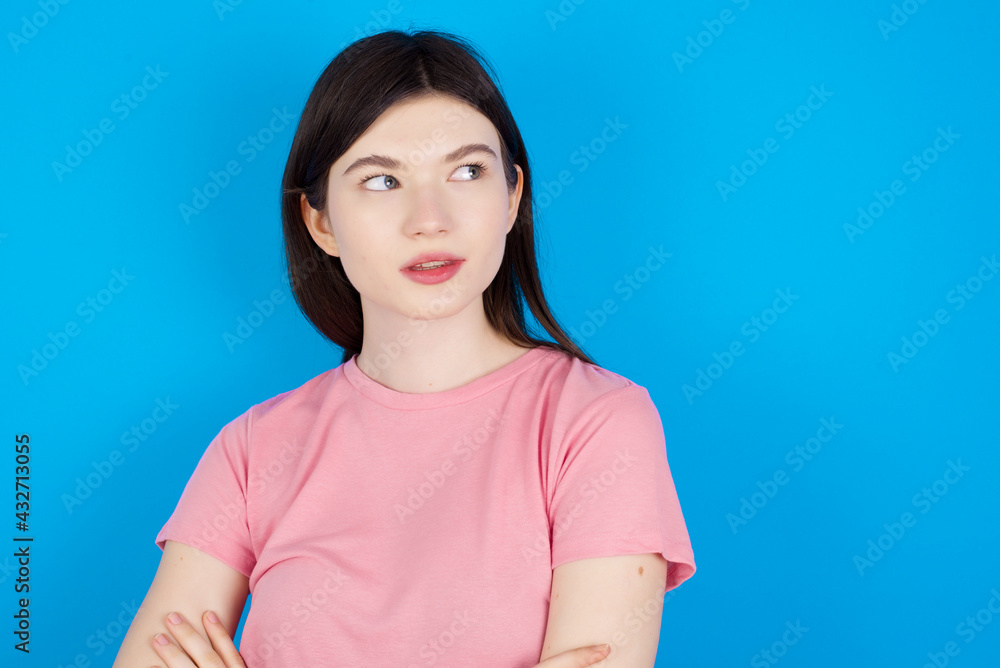 young beautiful Caucasian woman wearing pink T-shirt over blue wall looking aside into empty space thoughtful young beautiful Caucasian woman wearing pink T-shirt over blue wall looking aside into empty space thoughtful