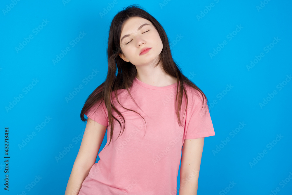 young beautiful Caucasian woman wearing pink T-shirt over blue wall looking sleepy and tired, exhausted for fatigue and hangover, lazy eyes in the morning. young beautiful Caucasian woman wearing pink T-shirt over blue wall looking sleepy and tired, exhausted for fatigue and hangover, lazy eyes in the morning.
