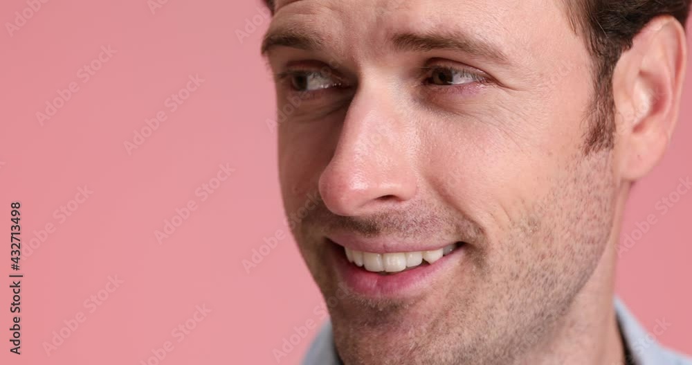 face close up of attractive unshaved man smiling, looking to side and nodding on pink background in studio face close up of attractive unshaved man smiling, looking to side and nodding on pink background in studio