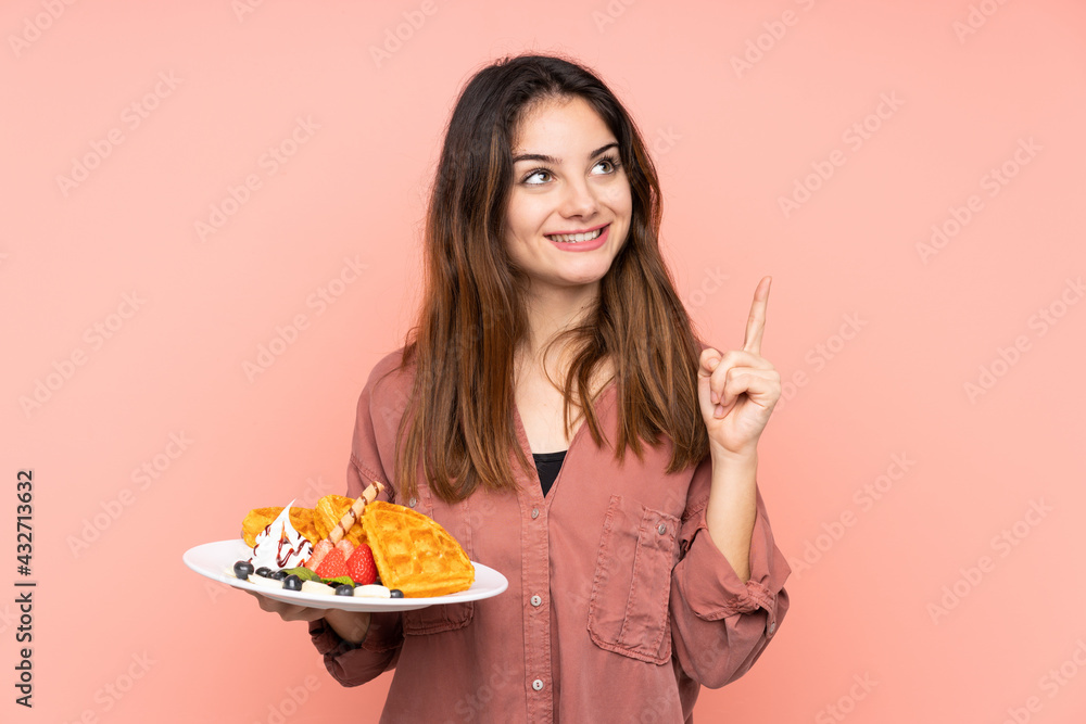 Young caucasian woman holding waffles isolated on pink background intending to realizes the solution while lifting a finger up Young caucasian woman holding waffles isolated on pink background intending to realizes the solution while lifting a finger up