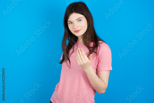 young beautiful Caucasian woman wearing pink T-shirt over blue wall inviting to come with hand. Happy that you came