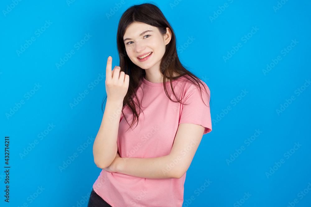 young beautiful Caucasian woman wearing pink T-shirt over blue wall Beckoning come here gesture with hand inviting welcoming happy and smiling young beautiful Caucasian woman wearing pink T-shirt over blue wall Beckoning come here gesture with hand inviting welcoming happy and smiling