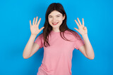 young beautiful Caucasian woman wearing pink T-shirt over blue wall showing and pointing up with fingers number nine while smiling confident and happy.