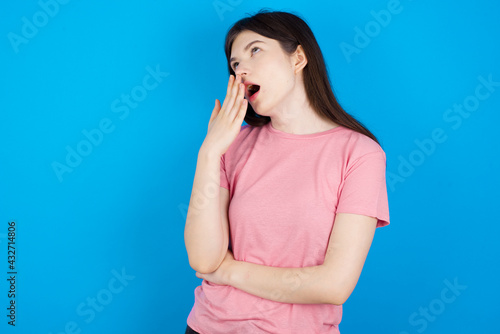 young beautiful Caucasian woman wearing pink T-shirt over blue wall being tired and yawning after spending all day at work.