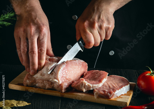 Chef or cook cutting meat with knife on kitchen, cooking food. Vegetables and spices on the kitchen table to prepare a delicious lunch