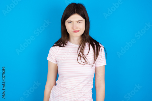 Offended dissatisfied young beautiful Caucasian woman wearing stripped T-shirt over blue wall with moody displeased expression at camera being disappointed by something