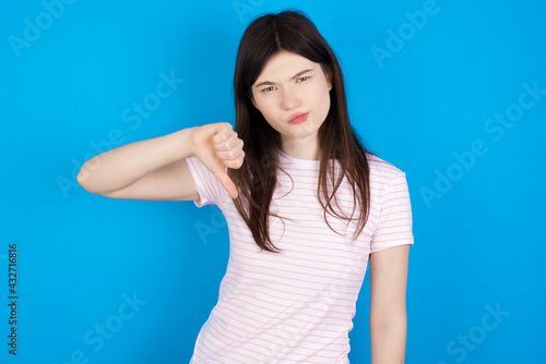 young beautiful Caucasian woman wearing stripped T-shirt over blue wall looking unhappy and angry showing rejection and negative with thumbs down gesture. Bad expression.