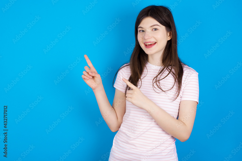 young beautiful Caucasian woman wearing stripped T-shirt over blue wall points at copy space indicates for advertising gives right direction young beautiful Caucasian woman wearing stripped T-shirt over blue wall points at copy space indicates for advertising gives right direction