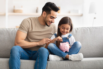 Little girl and dad saving money in piggy bank