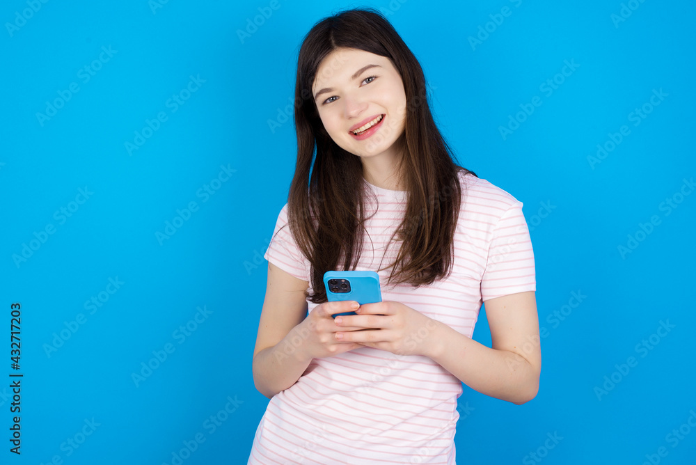 young beautiful Caucasian woman wearing stripped T-shirt over blue wall Mock up copy space. Using mobile phone, typing sms message young beautiful Caucasian woman wearing stripped T-shirt over blue wall Mock up copy space. Using mobile phone, typing sms message