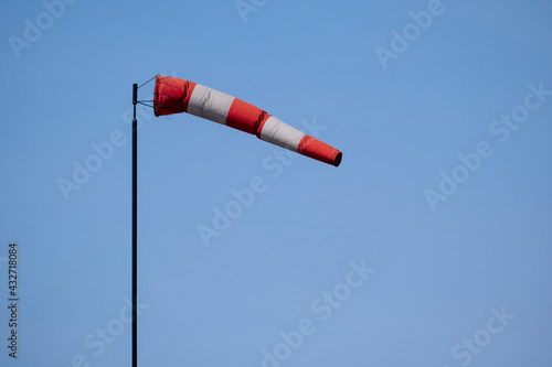 Closeup of striped windsock waiving in the wind against bright blue sky.