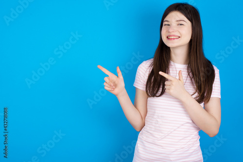 Optimistic young beautiful Caucasian woman wearing stripped T-shirt over blue wall points with both hands and  looking at empty space.