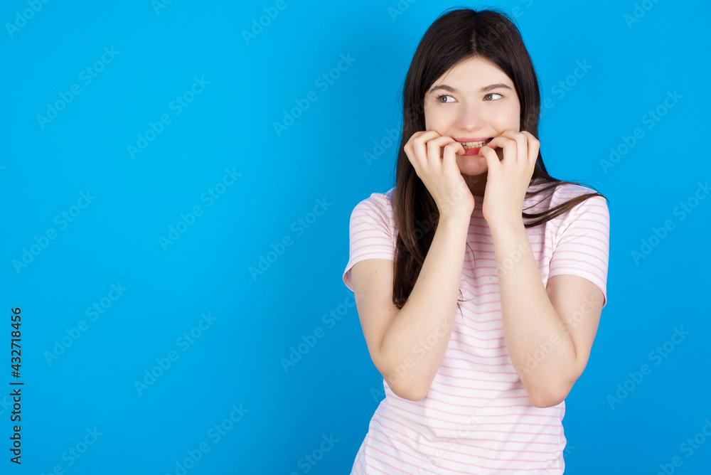 Terrified young beautiful Caucasian woman wearing stripped T-shirt over blue wall looks empty space home alone moonless night Terrified young beautiful Caucasian woman wearing stripped T-shirt over blue wall looks empty space home alone moonless night