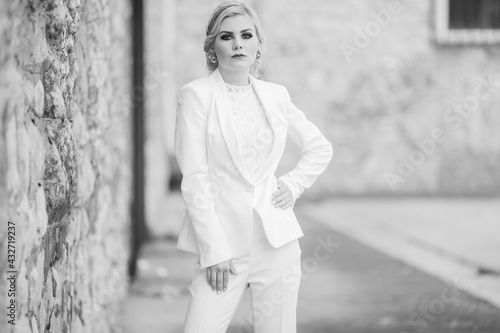 Tablou pe pânză Greyscale shot of a blonde female posing in an elegant white pantsuit