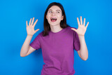 young beautiful Caucasian woman wearing purple T-shirt over blue wall showing and pointing up with fingers number ten while smiling confident and happy.