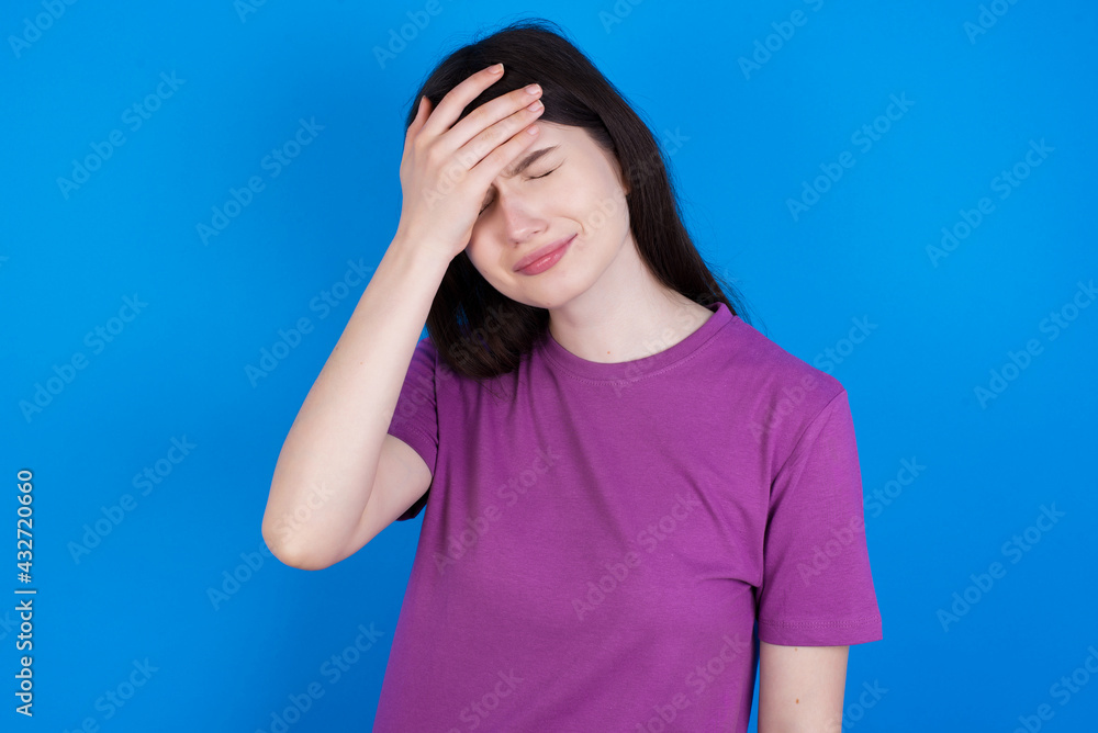 A very upset and lonely young beautiful Caucasian woman wearing purple T-shirt over blue wall crying, A very upset and lonely young beautiful Caucasian woman wearing purple T-shirt over blue wall crying,