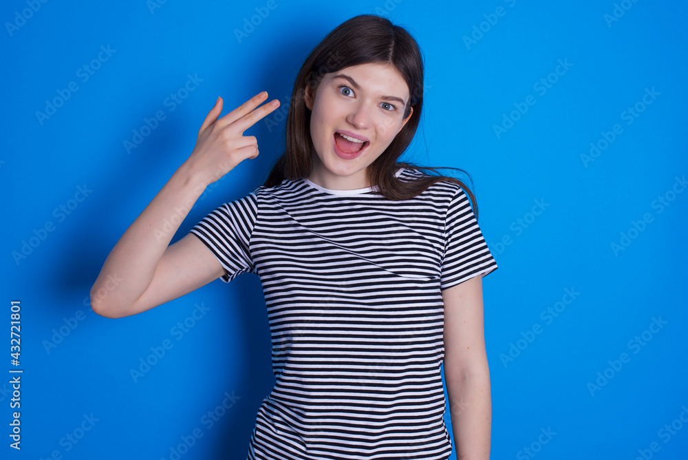 young beautiful Caucasian woman wearing pink jacket over blue wall foolishes around shoots in temple with fingers makes suicide gesture. Funny model makes finger gun pistol young beautiful Caucasian woman wearing pink jacket over blue wall foolishes around shoots in temple with fingers makes suicide gesture. Funny model makes finger gun pistol