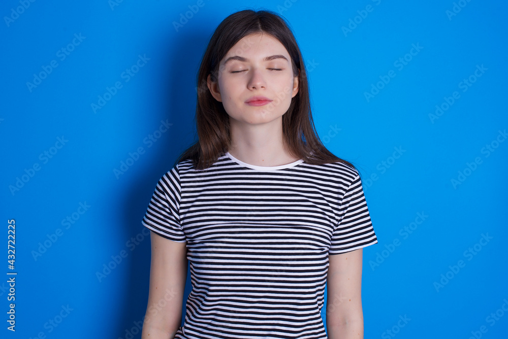 young beautiful Caucasian woman wearing stripped T-shirt over blue wall nice-looking sweet charming cute attractive lovely winsome sweet peaceful closed eyes young beautiful Caucasian woman wearing stripped T-shirt over blue wall nice-looking sweet charming cute attractive lovely winsome sweet peaceful closed eyes
