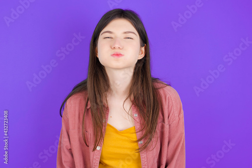 young beautiful Caucasian woman wearing casual clothes over purple wall puffing cheeks with funny face. Mouth inflated with air, crazy expression.