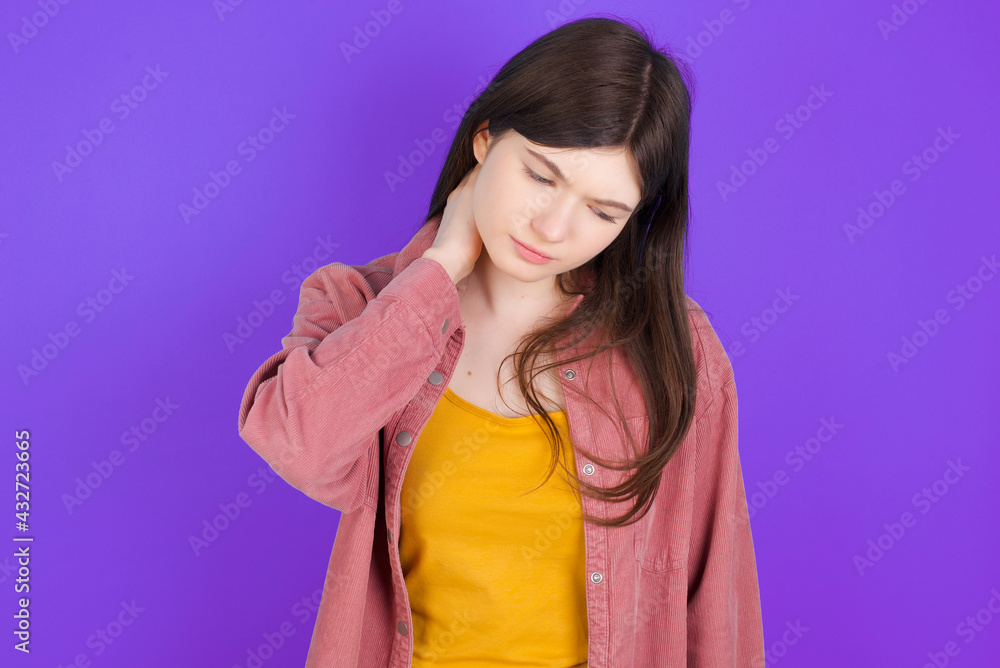 young beautiful Caucasian woman wearing casual clothes over purple wall suffering from back and neck ache injury, touching neck with hand, muscular pain. young beautiful Caucasian woman wearing casual clothes over purple wall suffering from back and neck ache injury, touching neck with hand, muscular pain.