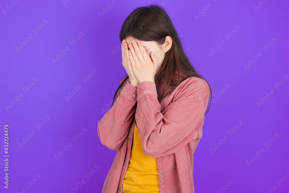 Sad young beautiful Caucasian woman wearing casual clothes over purple wall covering face with hands and crying. Sad young beautiful Caucasian woman wearing casual clothes over purple wall covering face with hands and crying.