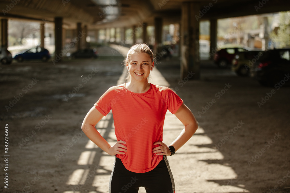Blonde girl runner looking at the camera, posing with hands on hips and smiling.