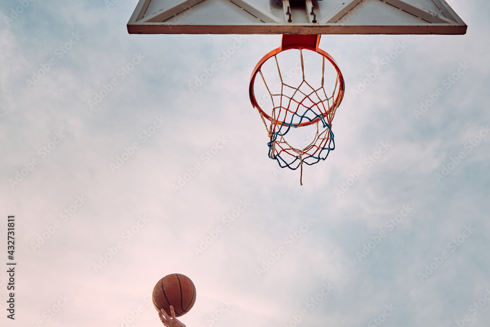 Hand of man throwing basketball to the basket hoop. Bottom up view of basketball hoop and ball against cloudy sky Hand of man throwing basketball to the basket hoop. Bottom up view of basketball hoop and ball against cloudy sky