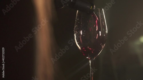 A girl pours red wine into a glass (back view, close-up, slow motion romantic setting in a dark room.