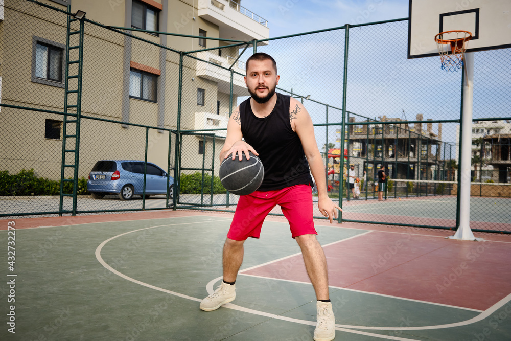 Young adult man plays basketball at outdoor court. Basketball player shows his dribbling skill