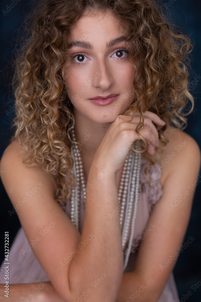 An attractive young woman with curly hair wearing a pink vintage evening dress and multiple pearl necklaces