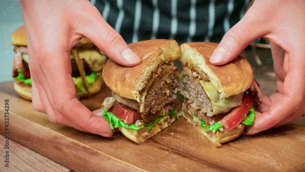 Close-up beef burger being sliced in half on the table in 4K. Serving burger from beef steak mince, sauce, bun, caramelised onions, cheese, tomato, lettuce. Close-up beef burger being sliced in half on the table in 4K. Serving burger from beef steak mince, sauce, bun, caramelised onions, cheese, tomato, lettuce.