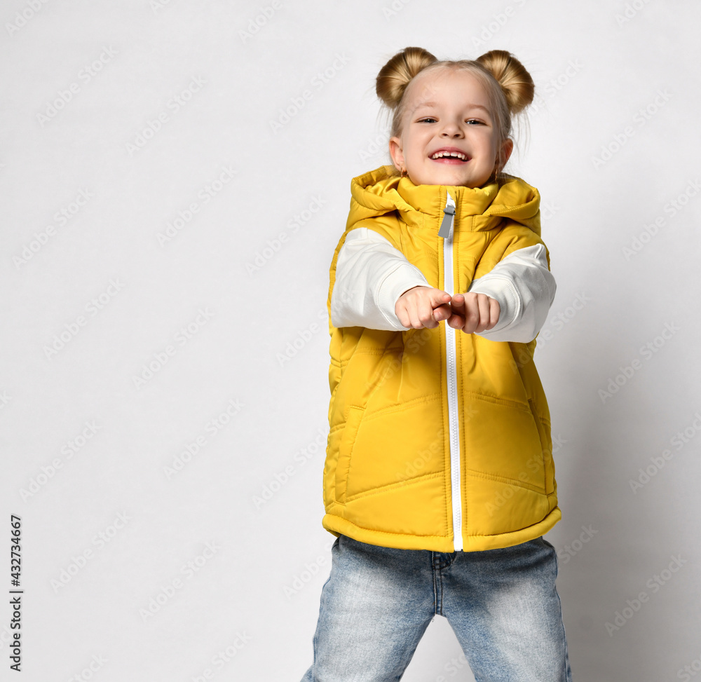 pretty smiling blonde in a yellow puffy vest is standing with her arms outstretched towards you. pretty smiling blonde in a yellow puffy vest is standing with her arms outstretched towards you.