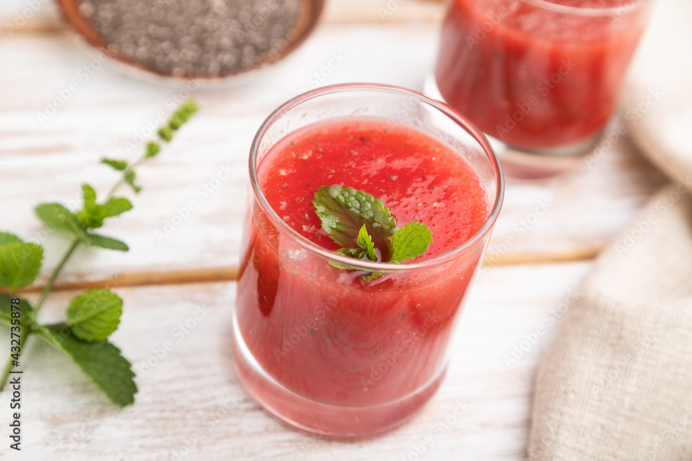 Watermelon juice with chia seeds and mint in glass on a white wooden background with linen textile. Side view, selective focus. Watermelon juice with chia seeds and mint in glass on a white wooden background with linen textile. Side view, selective focus.