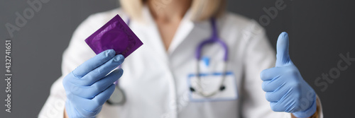 Doctor holding condom in his hands and showing thumb up closeup photo