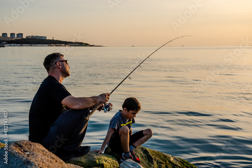 A fisherman sits on a rock by the sea with a fishing rod at sunset. Single sea fishing. Day at the beach. Copy space for text