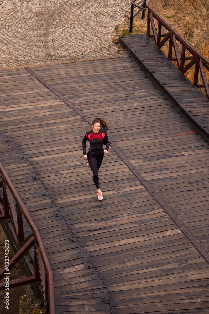 landscape, one young woman running, jogging outdoors over a wood bridge.